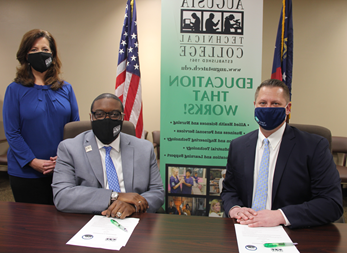 Caucasian male wearing a blue face mask, blue suit jacket, white collared shirt, light blue tie, hands folded while sitting down at a table, white paper in front of him with a green pen; African American male wearing a black Augusta Tech branded face mask, light gray suit, silver Augusta Tech lapel pin, white collared shirt, blue/purple tie, silver watch, hands folded white sitting at a brown table, white papers on brown table in front of him with a green pen; Caucasian female standing wearing a black Augusta Tech branded face mask, blue shirt, hands folded together, black pants, background features an American flag, the state of Georgia flag, large retractable banner showing old Augusta Tech logo, verbiage reads: pzt9gyai.wbilshop.net, Education That Works; bulleted list reads Allied Health Sciences and Nursing, Business and Personal Services, and Engineering Technology, Industrial Technology, and Learning Support, photos underneath the bulleted list.