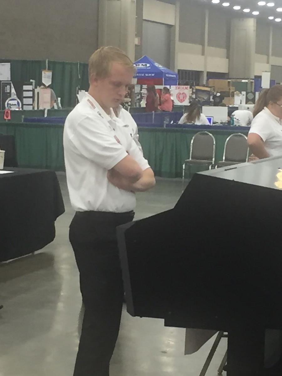 一个年轻的白人大学生，穿着白色polo衫和黑色西裤, Hunter Steed, 在比赛中低头盯着图形显示器.